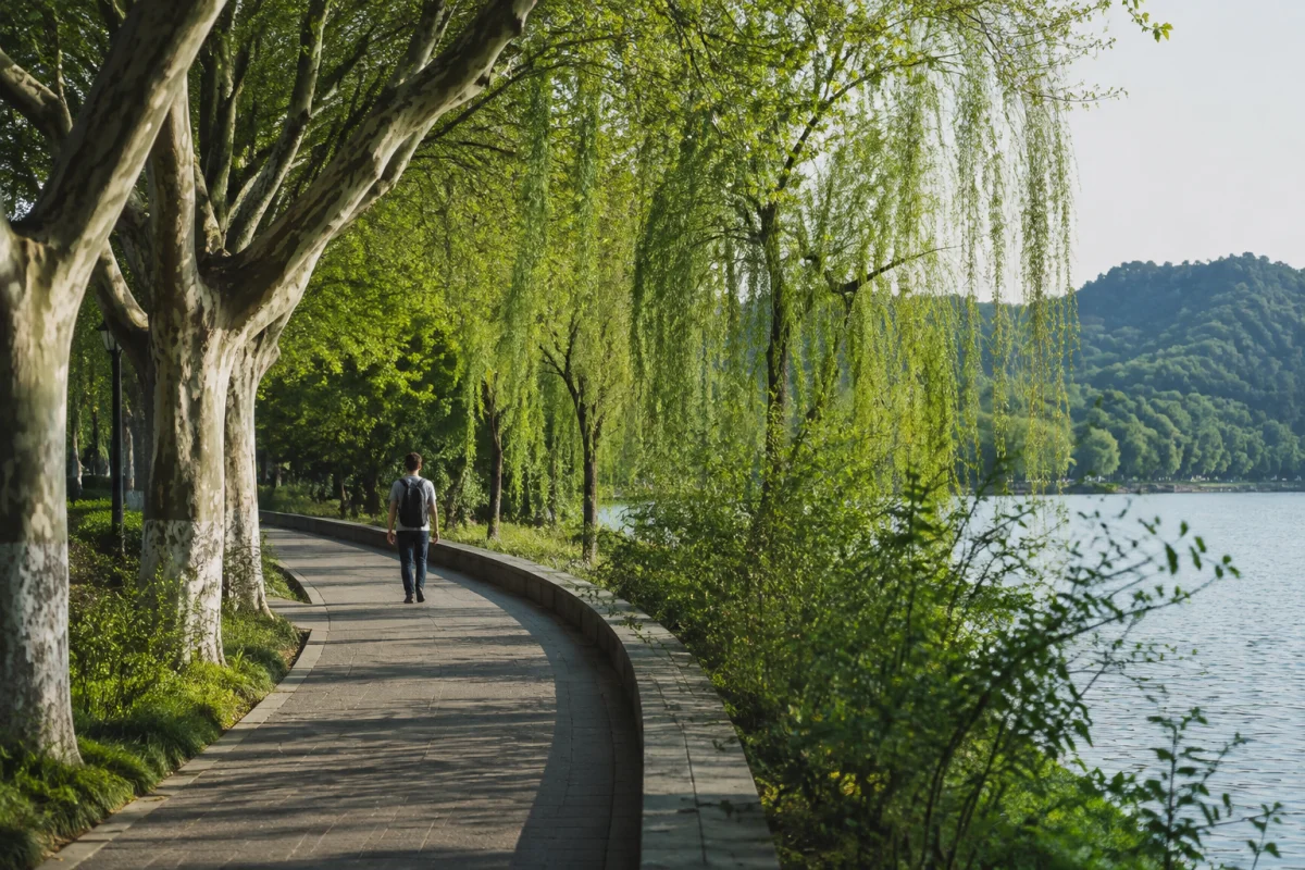 Traveler walking a shaded path beside West Lake in Hangzhou