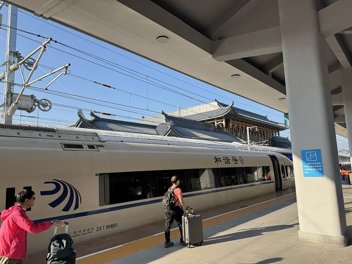 Travelers with luggage beside a high-speed train at Furong Town Railway Station